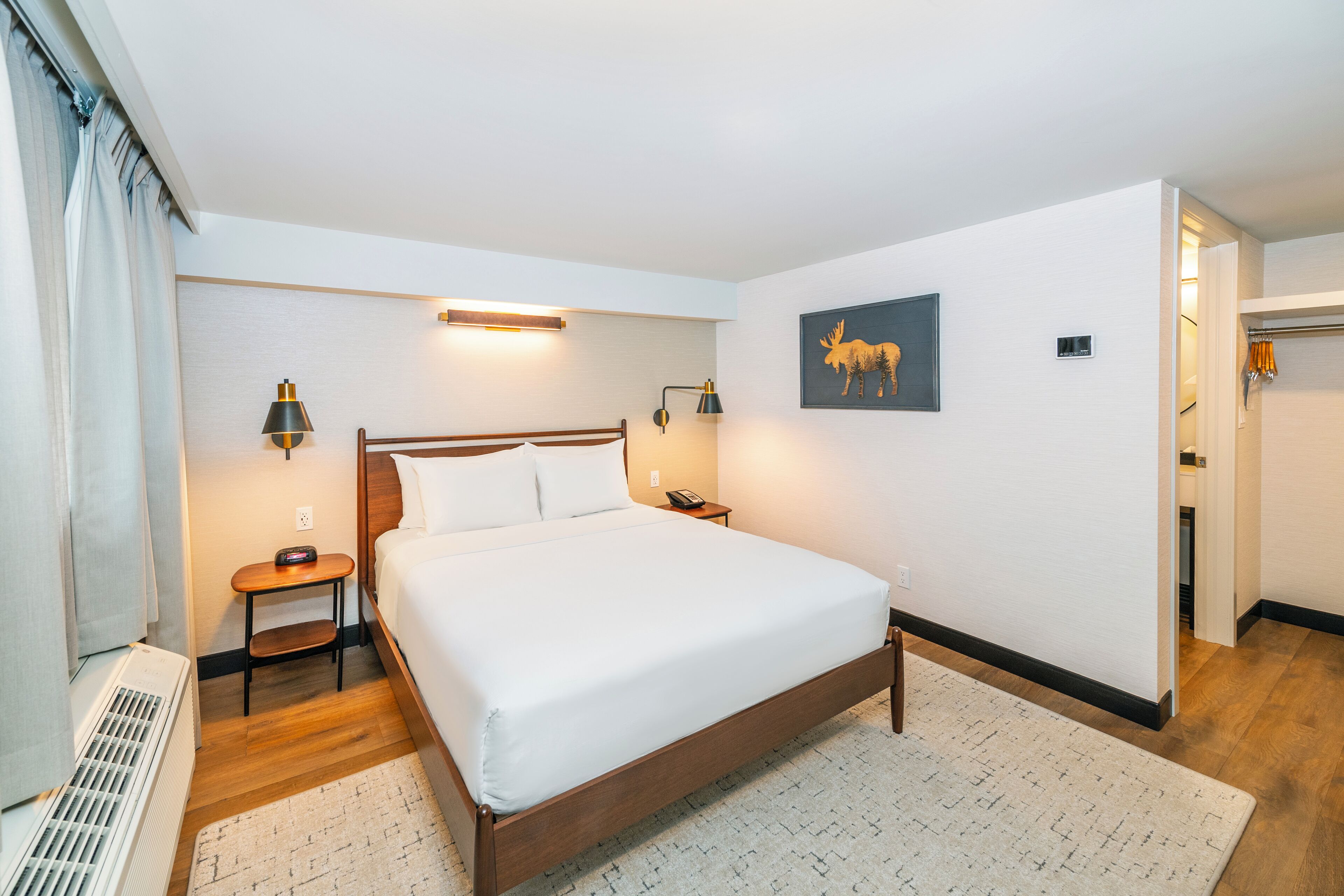 Habitació d'hotel ordenada amb un llit gran, làmpades de sobretaula, una obra penjada a la paret i una porta visible que dona a una altra habitació.