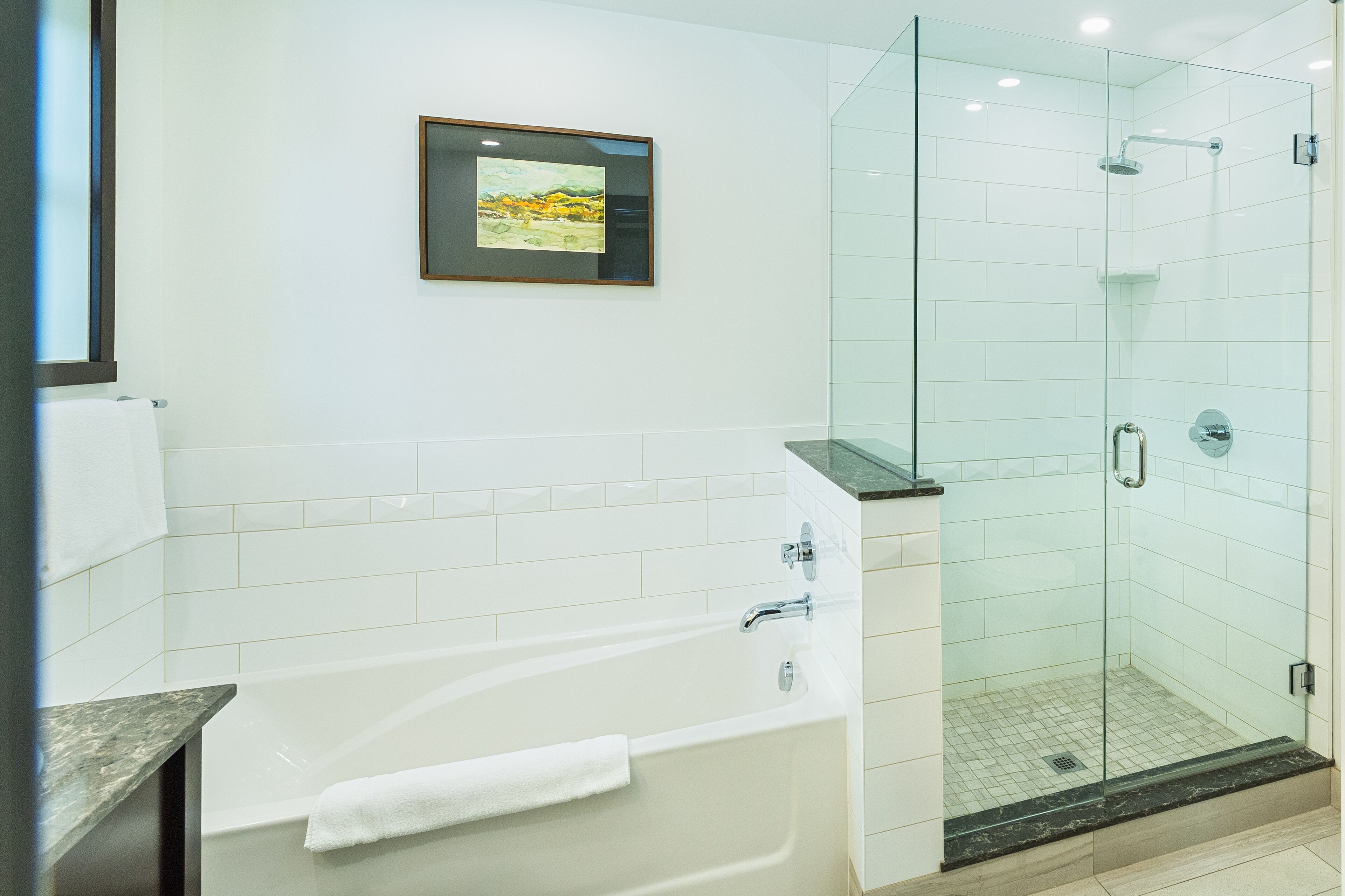 Un baño moderno con bañera, cabina de ducha de vidrio y un cuadro en la pared.