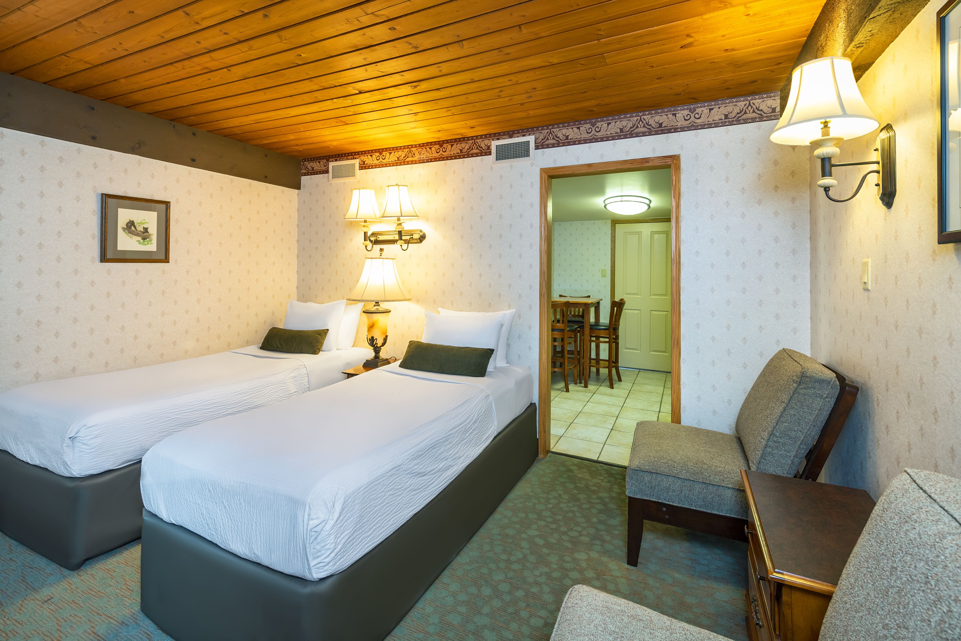 A room with two beds, a chair, a table, and a lamp.