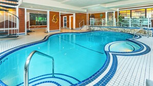 An indoor swimming pool with a blue tiled edge, a wooden deck area, and a glass wall with a view of the outdoors. - Charltons Banff (Banff)