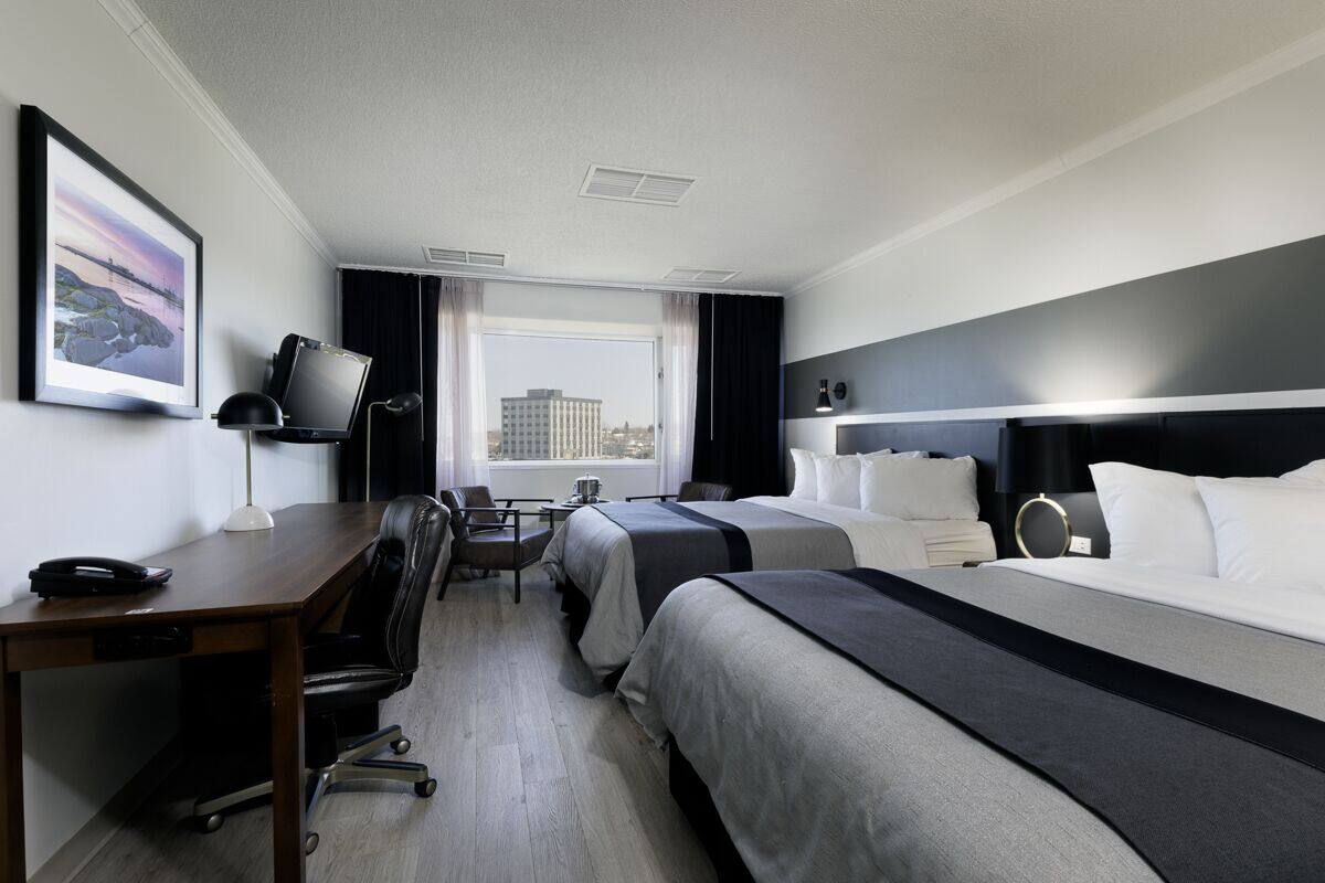 A hotel room with two beds, a desk with a chair, a TV, and a window with curtains.