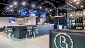 A modern bar area with a counter, bar stools, and a large illuminated logo. - Hotel Rimouski (Rimouski)