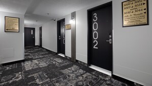 A hotel corridor with black doors numbered 3002, 3003, 3004, and 3005. There are signs indicating room numbers and a plaque with room amenities. - Hotel Rimouski (Rimouski)