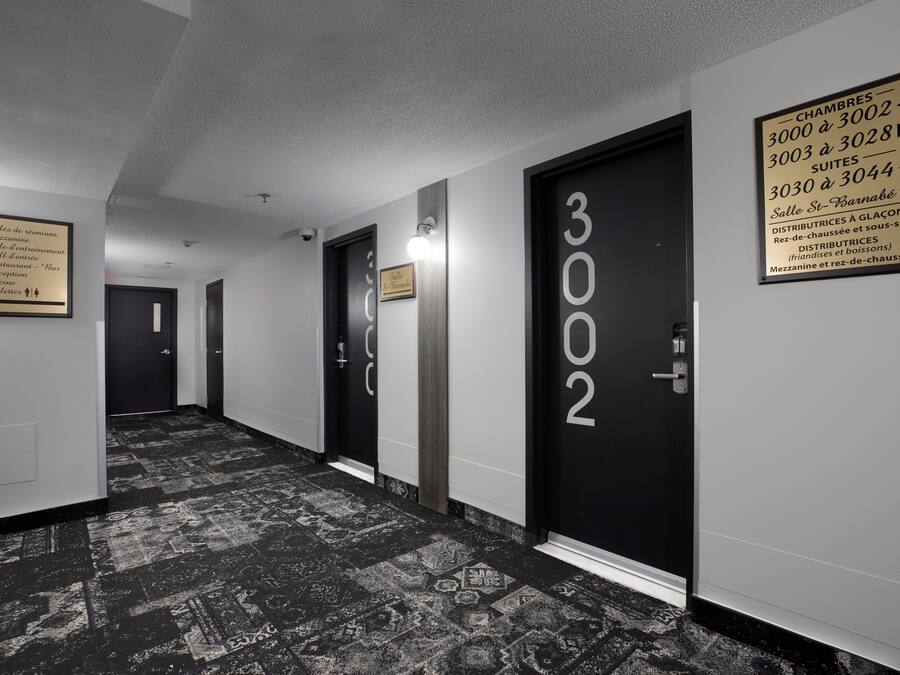 A hotel corridor with black doors numbered 3002, 3003, 3004, and 3005. There are signs indicating room numbers and a plaque with room amenities.