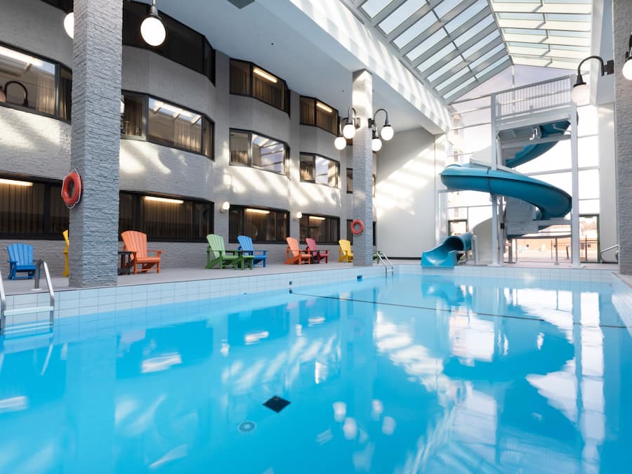 An indoor swimming pool with a water slide, multiple lounge chairs, and a high ceiling with skylights.