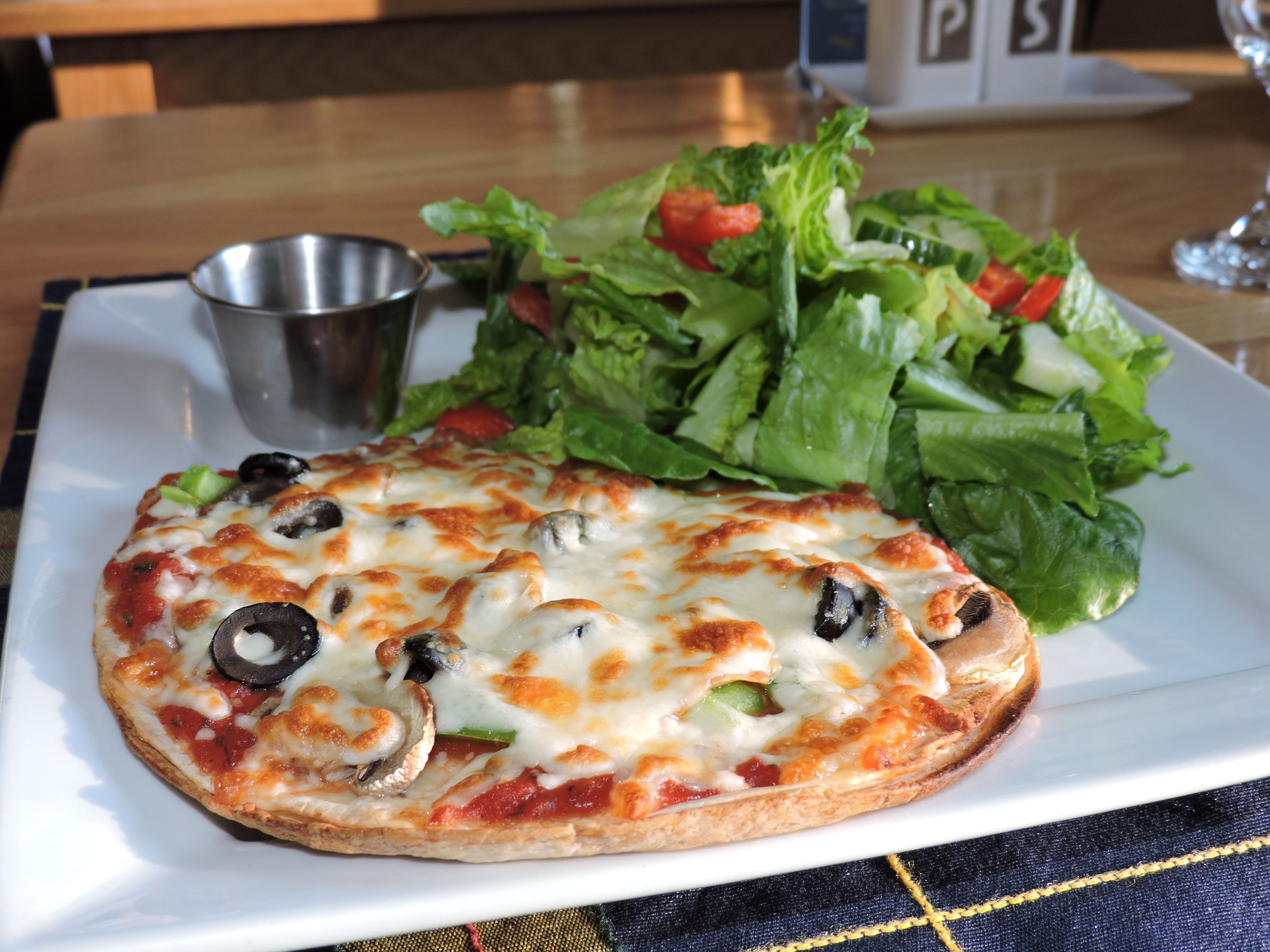 A pizza with toppings and a side salad on a white plate.