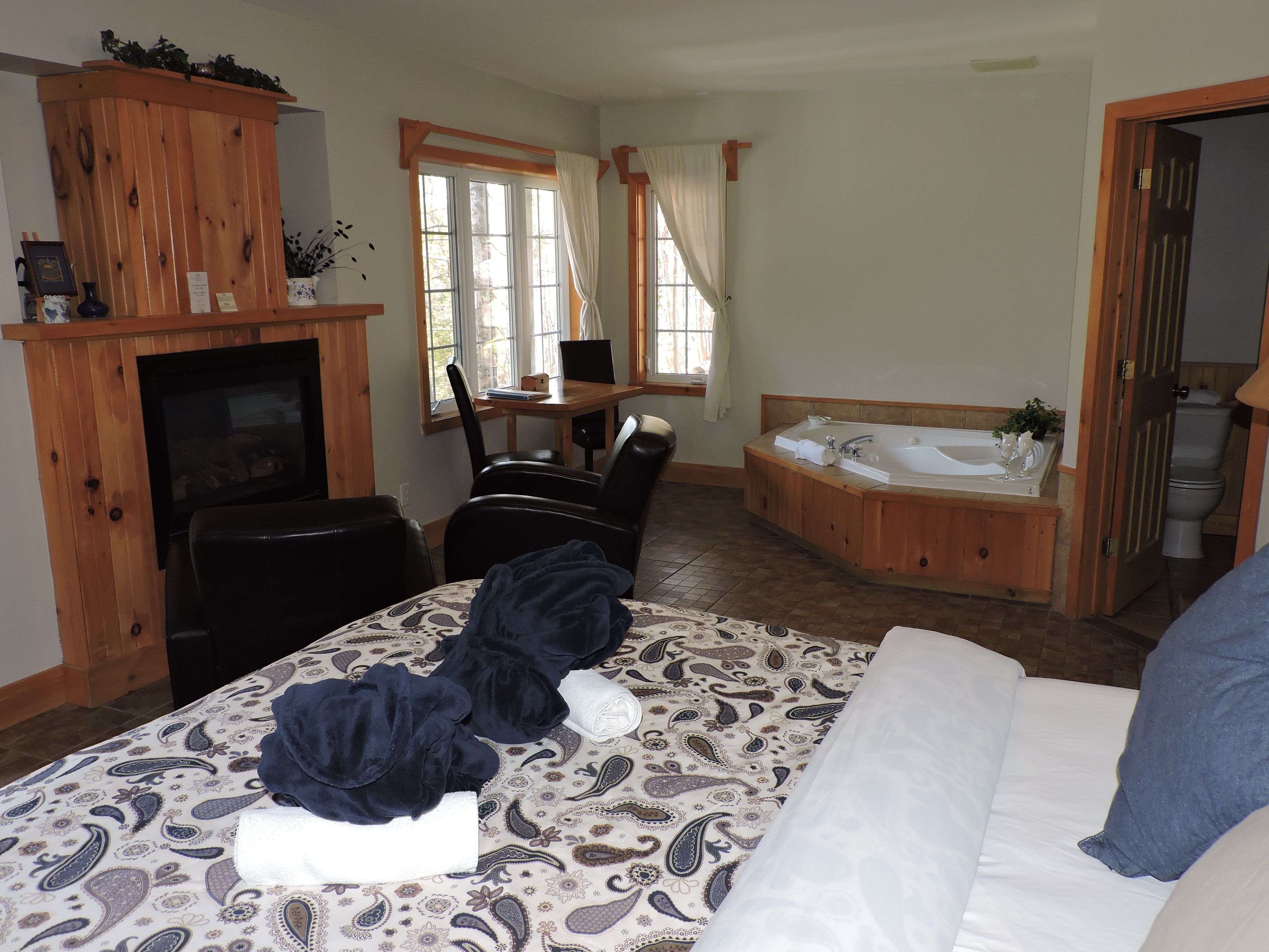 A bedroom with a bed, a wooden cabinet, a desk with a chair, a window with curtains, and a bathroom with a bathtub.