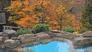Una piscina azul cristalina rodeada de rocas grandes y árboles de colores otoñales.