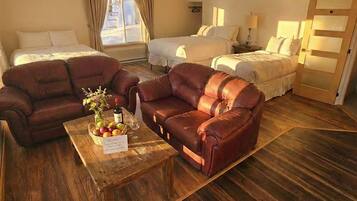 Ein Hotelzimmer mit zwei Betten, einem Sofa, einem Couchtisch mit Obst und einer Flasche sowie einem Holzboden.