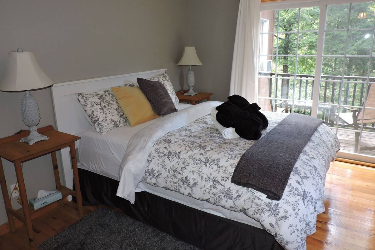 Quarto com cama, duas mesas de cabeceira, janela com vista e varanda.