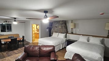 A hotel room with two beds, a dining area, a leather sofa, and a stone accent wall.