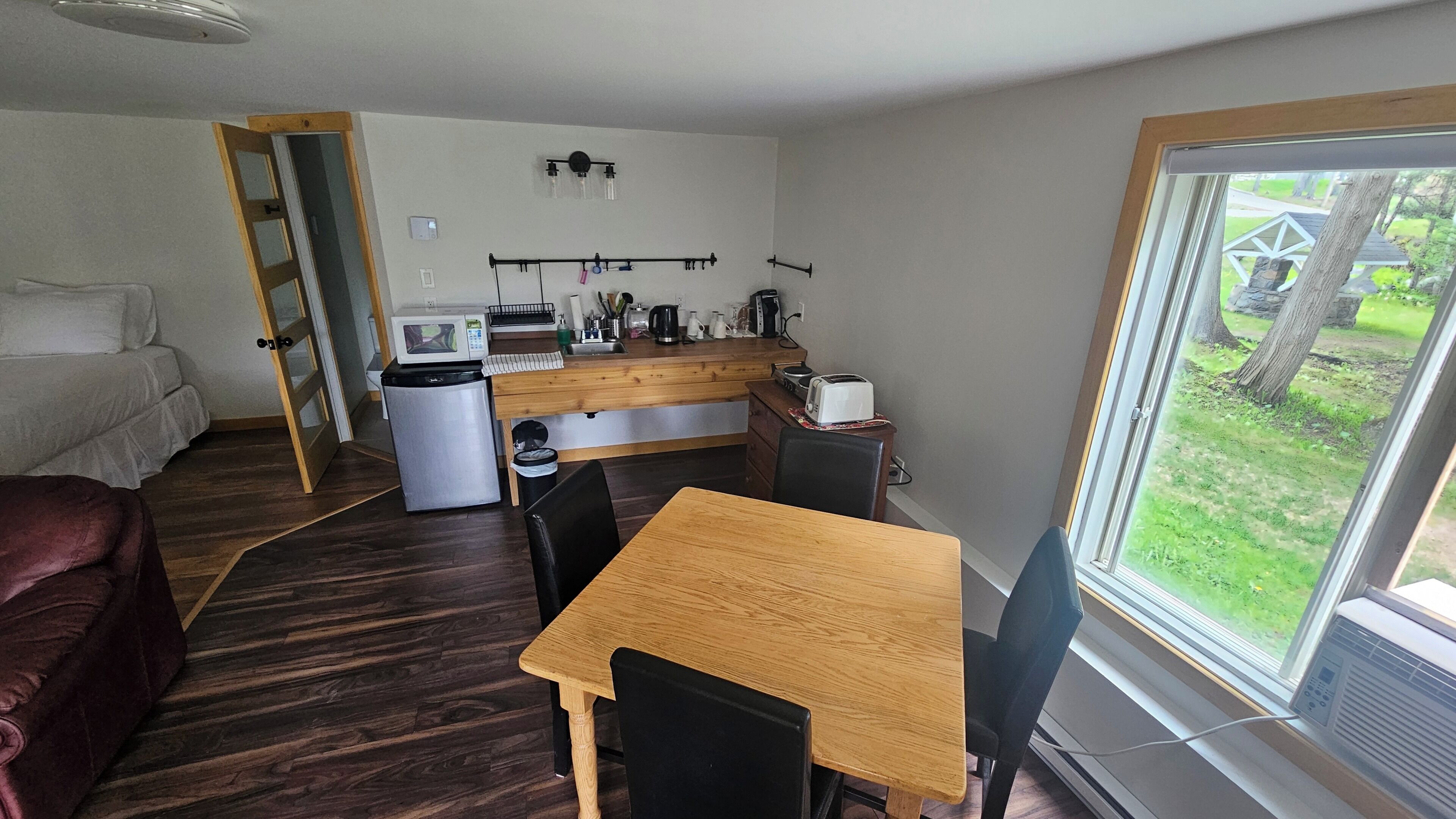 A compact living space with a kitchenette, a dining area, and a large window offering a view of the outdoors.