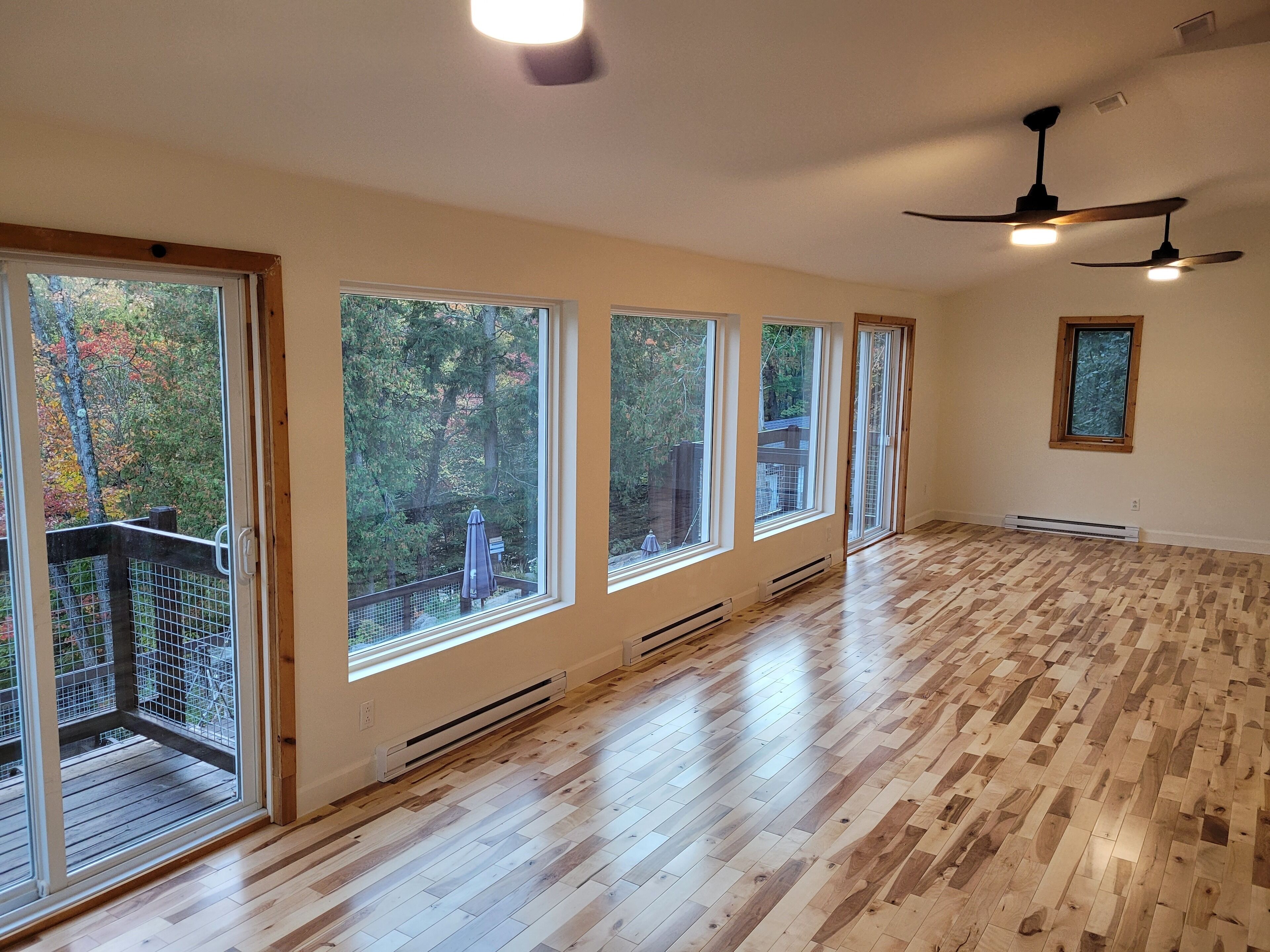 A spacious room with large windows, wooden flooring, and a ceiling fan.