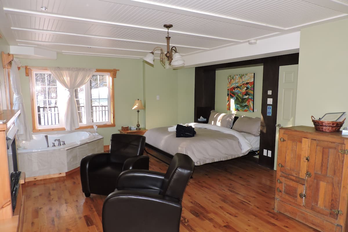 Um quarto com uma cama grande, cômoda de madeira, uma cadeira, mesa de cabeceira com abajur e janela com cortinas.