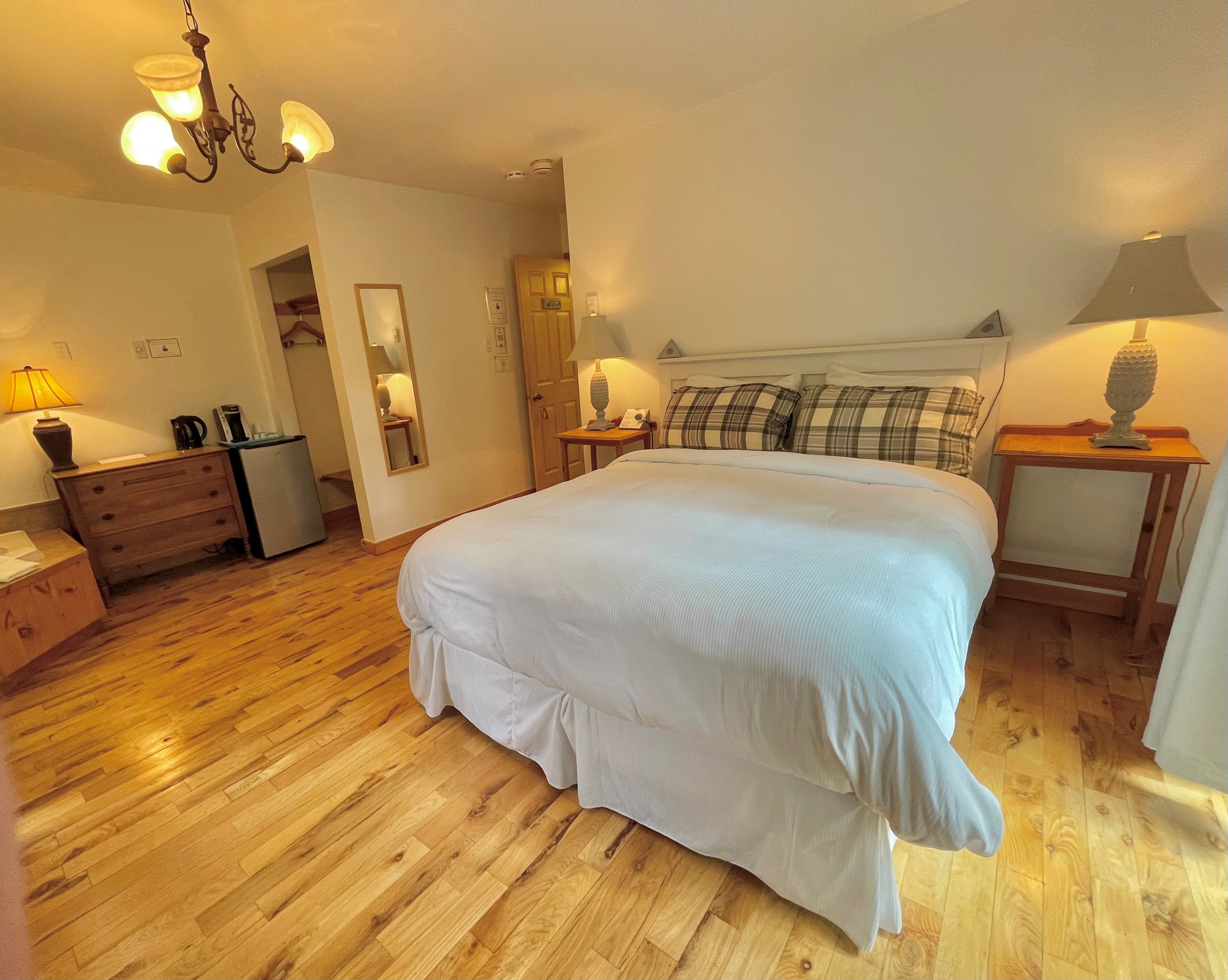 Un dormitorio con una cama grande, suelo de madera, un aparador, un espejo y una araña.
