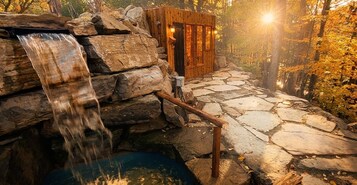 Una cabaña rústica de madera con un sendero de piedra que lleva a una cascada y un jacuzzi.
