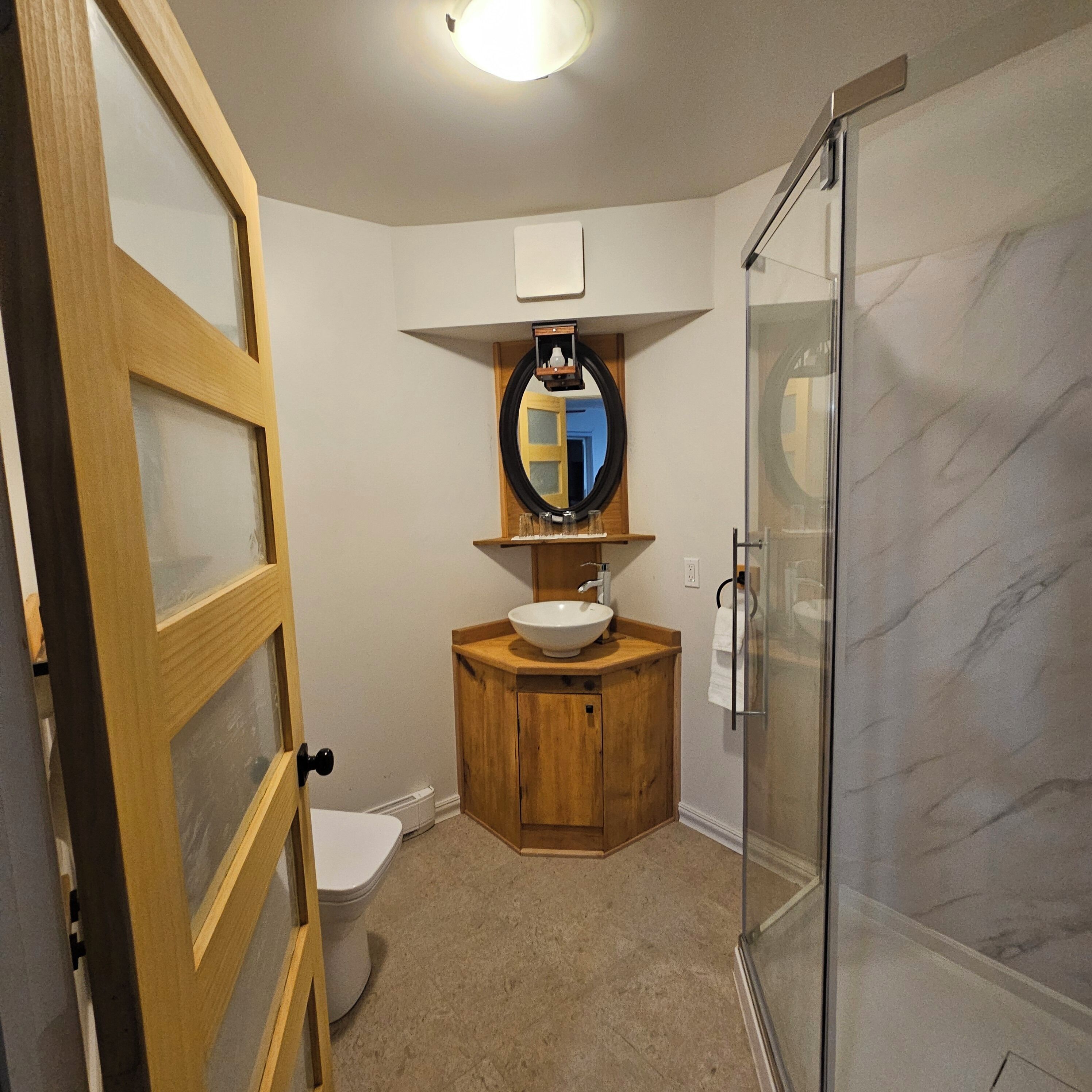 A bathroom with a wooden vanity, a white toilet, a glass shower enclosure, and a mirror above the sink.