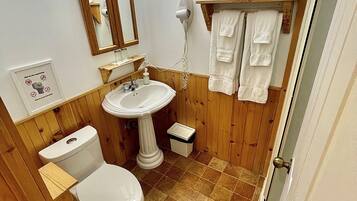 A bathroom with a pedestal sink, a toilet, a mirror, and a towel rack.