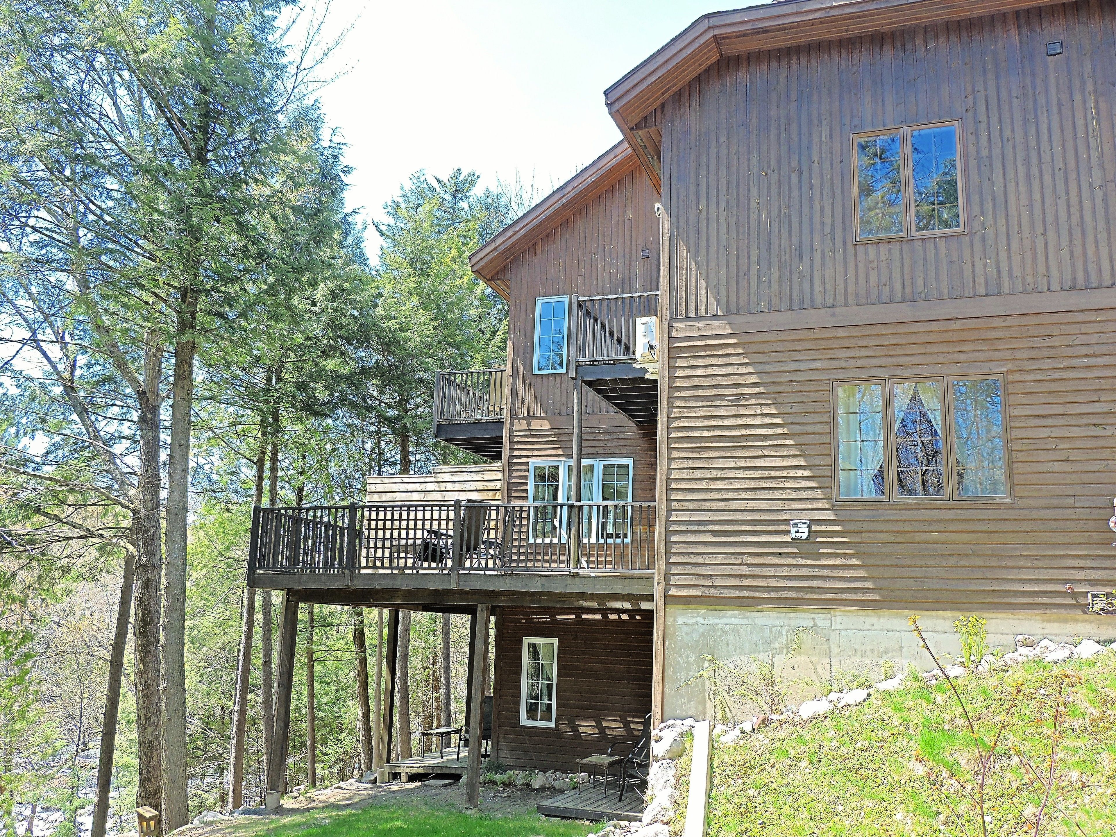 A two-story wooden cabin with a balcony, surrounded by trees.