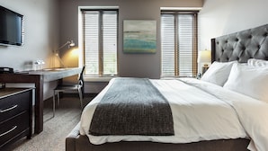 Una habitación de hotel con cama, escritorio, silla, televisión y dos ventanas con persianas.