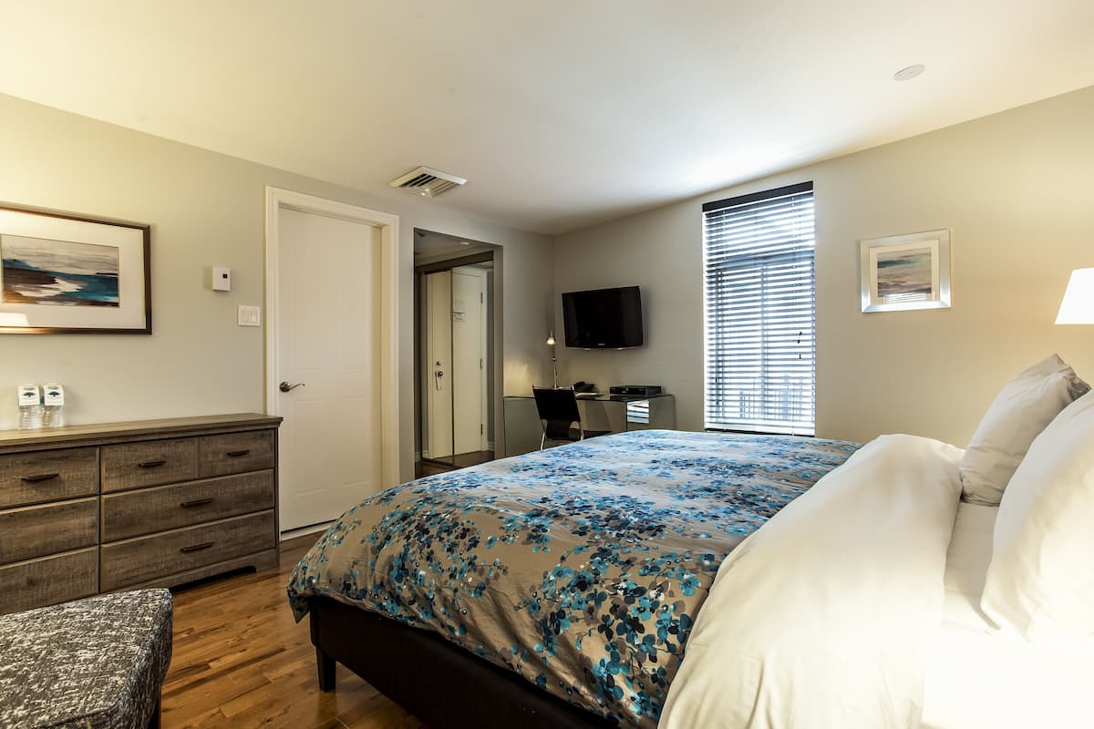 A bedroom with a bed, dresser, desk, and TV.
