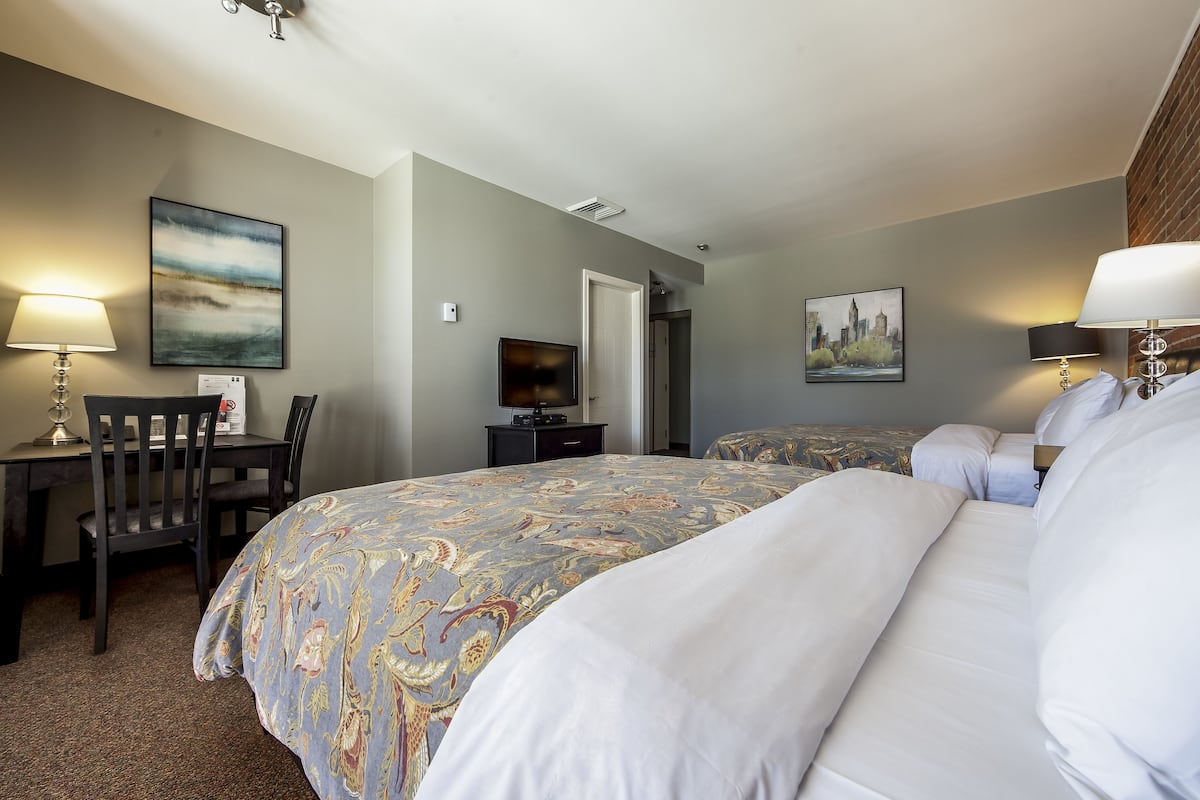 A hotel room with a large bed, a desk with a chair, a television, and two paintings on the walls.