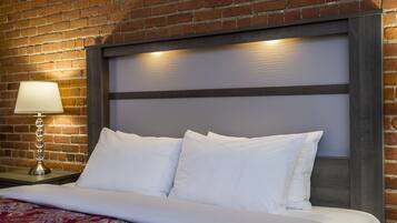 Una habitación de hotel con una pared de ladrillo, una cama con sábanas blancas y una mesita de noche con lámpara.