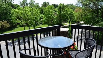 A balcony with a round glass table and two wicker chairs, surrounded by a black railing.