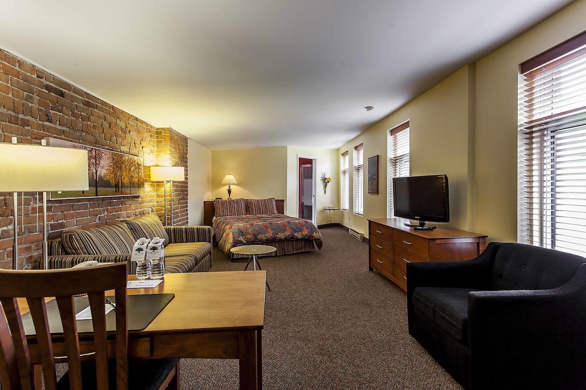 A hotel room with a brick wall, a bed, a sofa, a TV, and a desk.