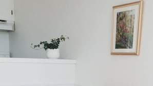 A dining area with a wooden table and chairs, a potted plant on a white shelf, and a framed picture on the wall.