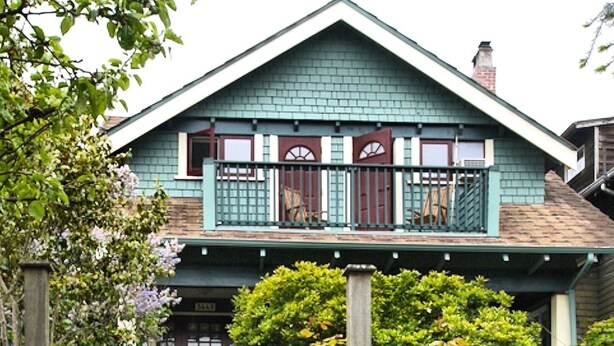 A two-story house with a front porch, a set of stairs leading to the entrance, and a small garden area with various plants. - A Suite at Kitsilano Cottage (Vancouver)