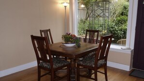A dining table with four chairs, a flower vase, and a window with a view of greenery. - A Suite at Kitsilano Cottage (Vancouver)