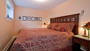 A bedroom with a large bed, a wooden headboard, a nightstand with a lamp, and framed pictures on the wall. - A Suite at Kitsilano Cottage (Vancouver)