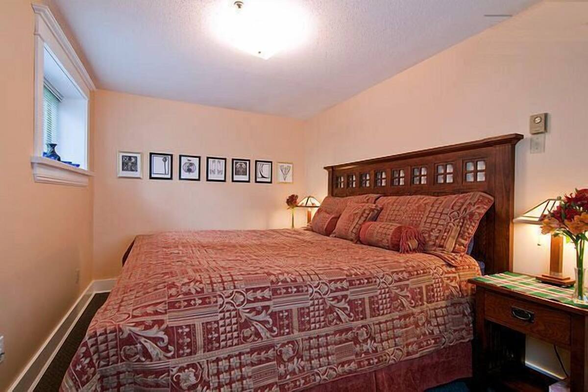 A bedroom with a large bed, a wooden headboard, a nightstand with a lamp, and framed pictures on the wall.