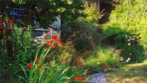 A garden with a variety of plants and flowers, a pathway, and a building in the background. - A Suite at Kitsilano Cottage (Vancouver)