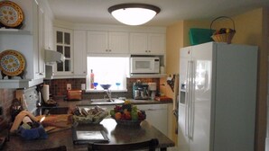 A kitchen with white cabinets, a microwave, a refrigerator, and a fruit bowl on the counter. - A Suite at Kitsilano Cottage (Vancouver)