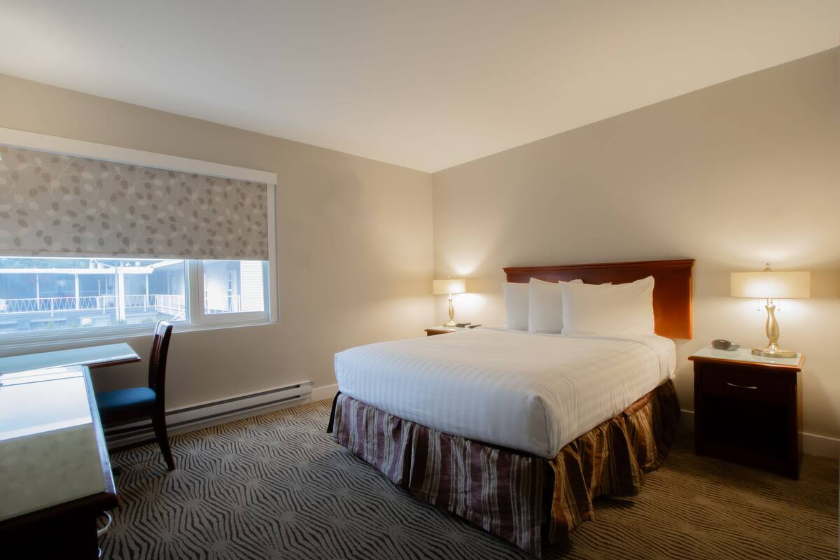 A hotel room with a bed, desk, chair, and a window with a view.