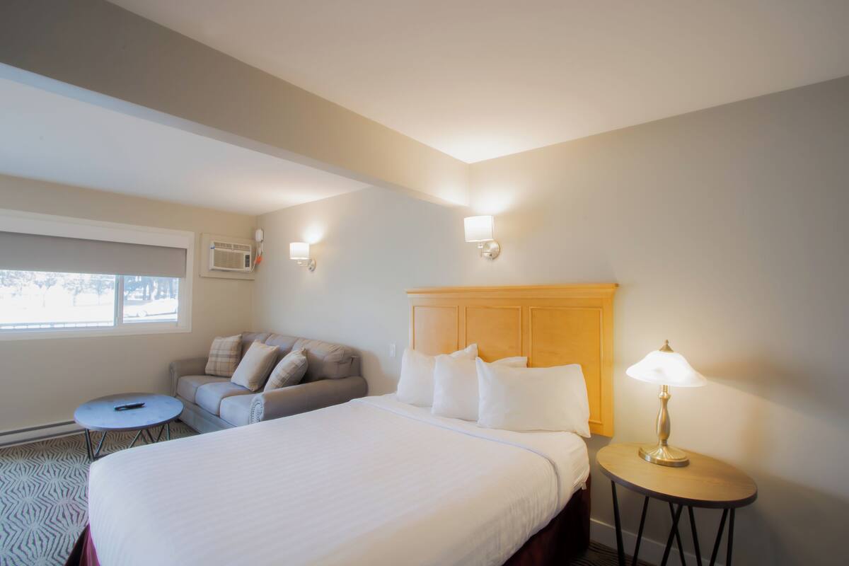 A hotel room with a large bed, a small round table, a sofa, and a lamp.