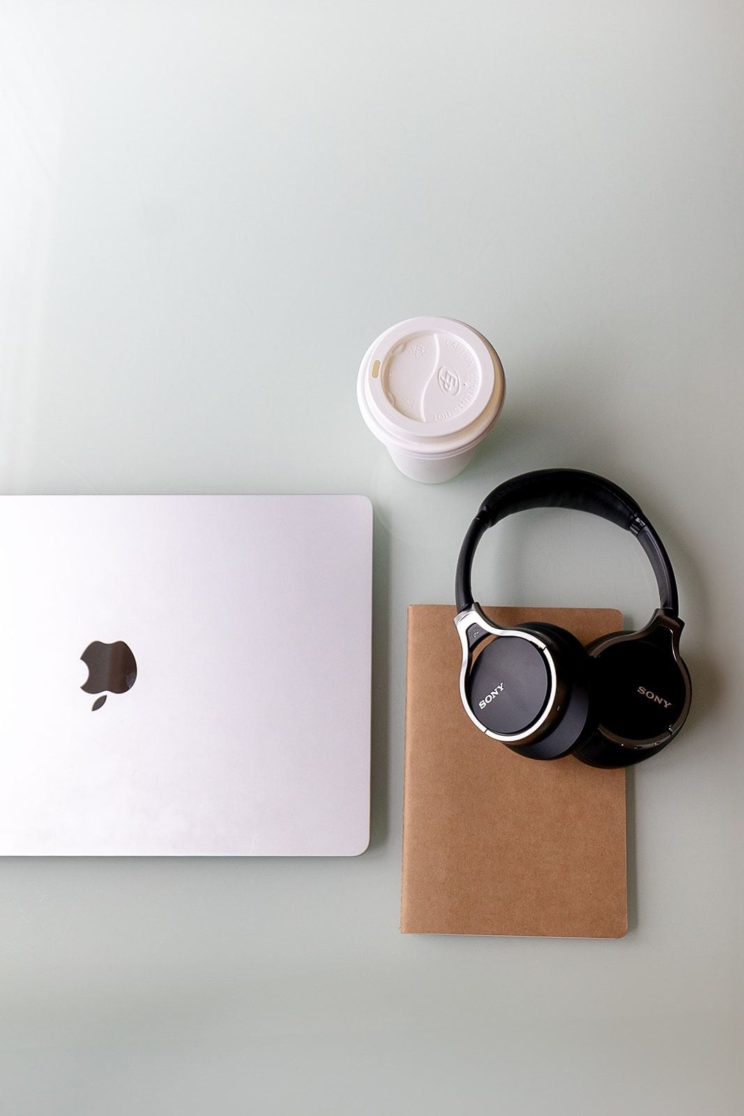 A laptop, headphones, and a coffee cup on a flat surface.