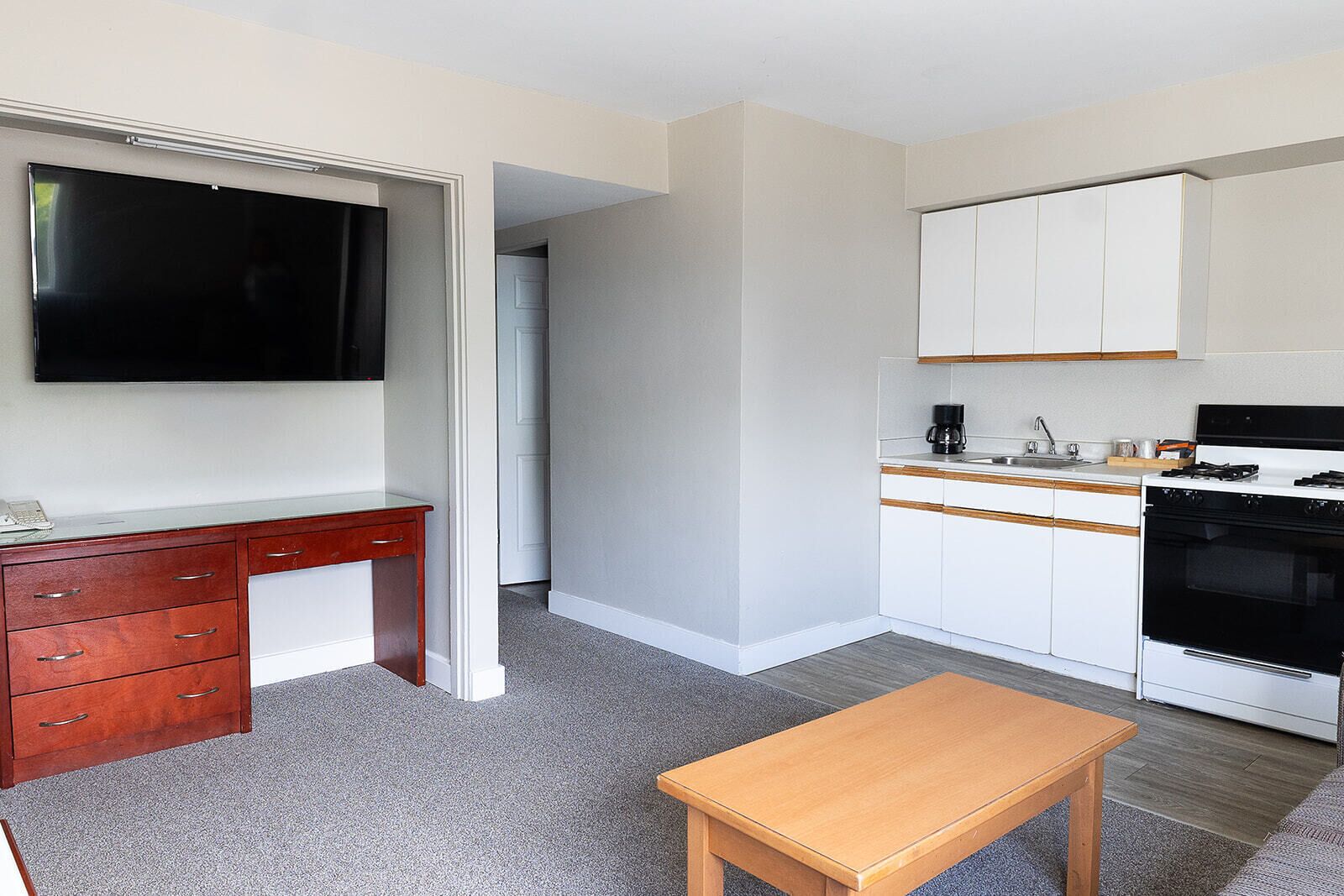 A compact kitchen with white cabinets, a black stove, and a wooden table.