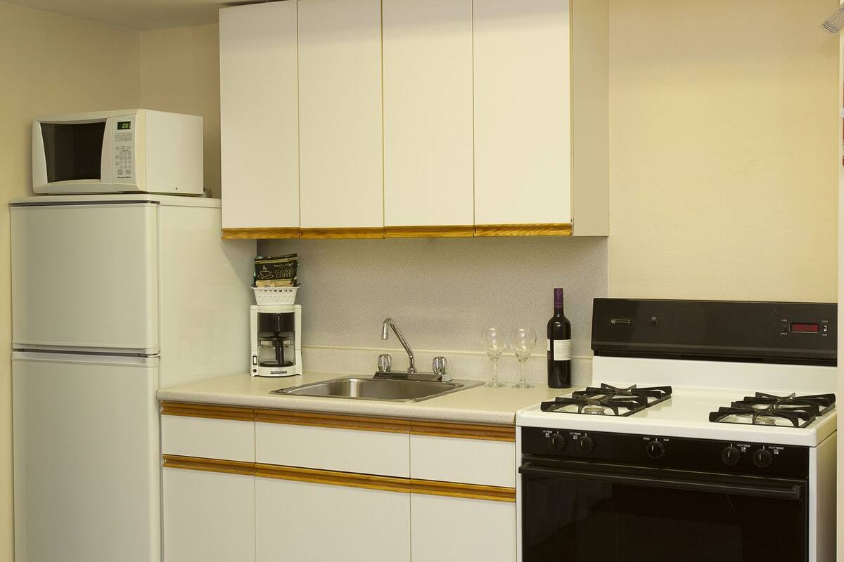 A kitchen with a microwave, coffee maker, sink, wine bottle, and stove.