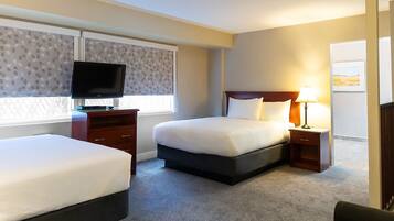 A hotel room with two beds, a TV, a bedside table with a lamp, and a window with patterned curtains.