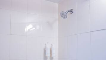A bathroom with white tiles, a showerhead, and two bottles of Terra Green hand soap.