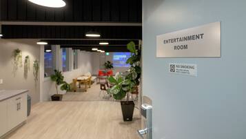 Un intérieur agrémenté d’un panneau indiquant « SALLE DE DIVERTISSEMENT », où il est interdit de fumer, et qui présente un espace moderne et bien éclairé, avec des plantes et du mobilier.