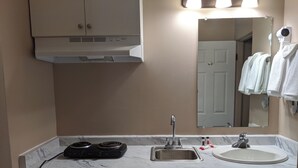Un baño con un lavamanos blanco, un espejo, un perchero para toallas y una estufa.