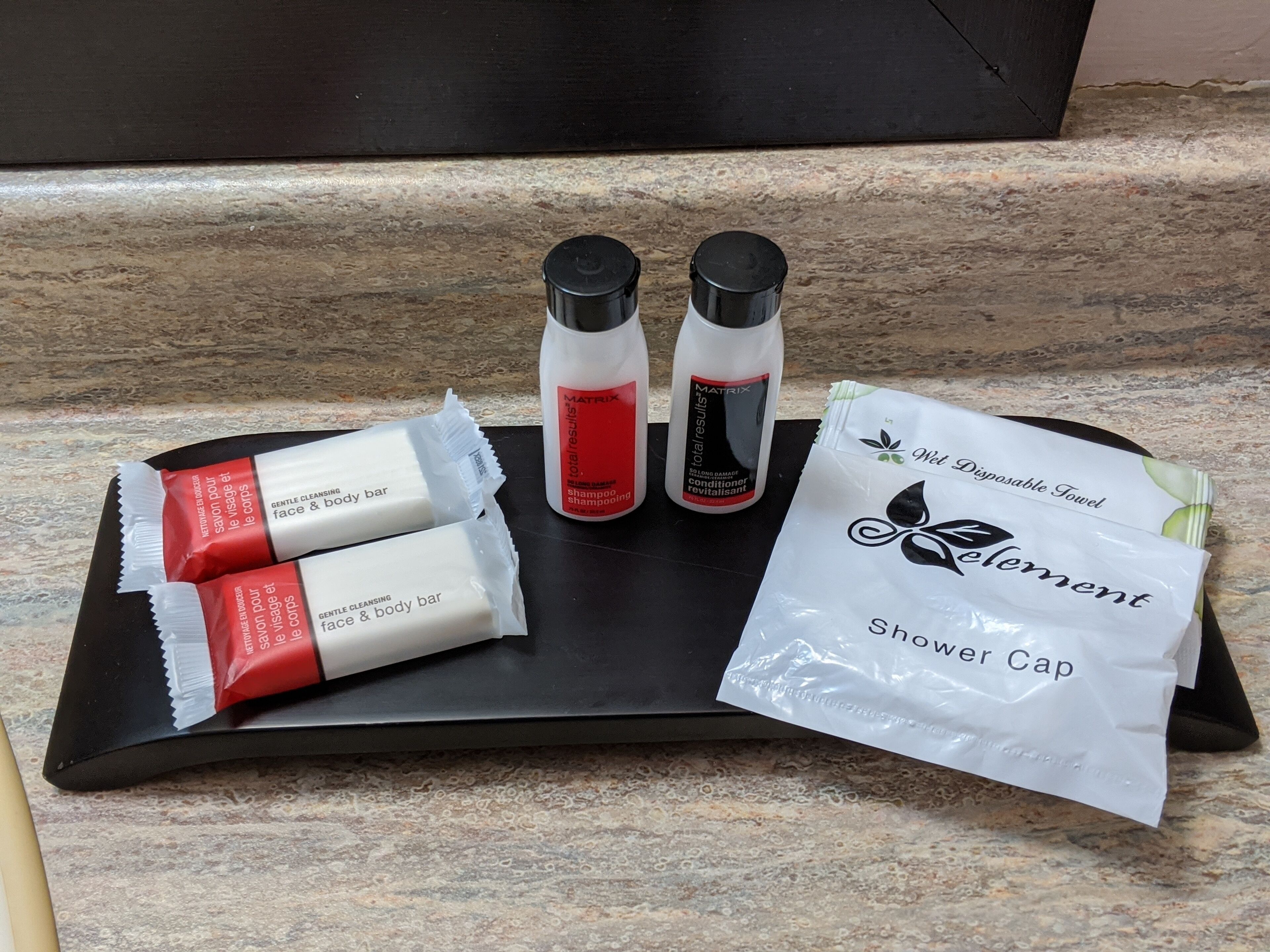 A tray with toiletries including a shower cap, a bar of soap, and two bottles of shampoo and conditioner.