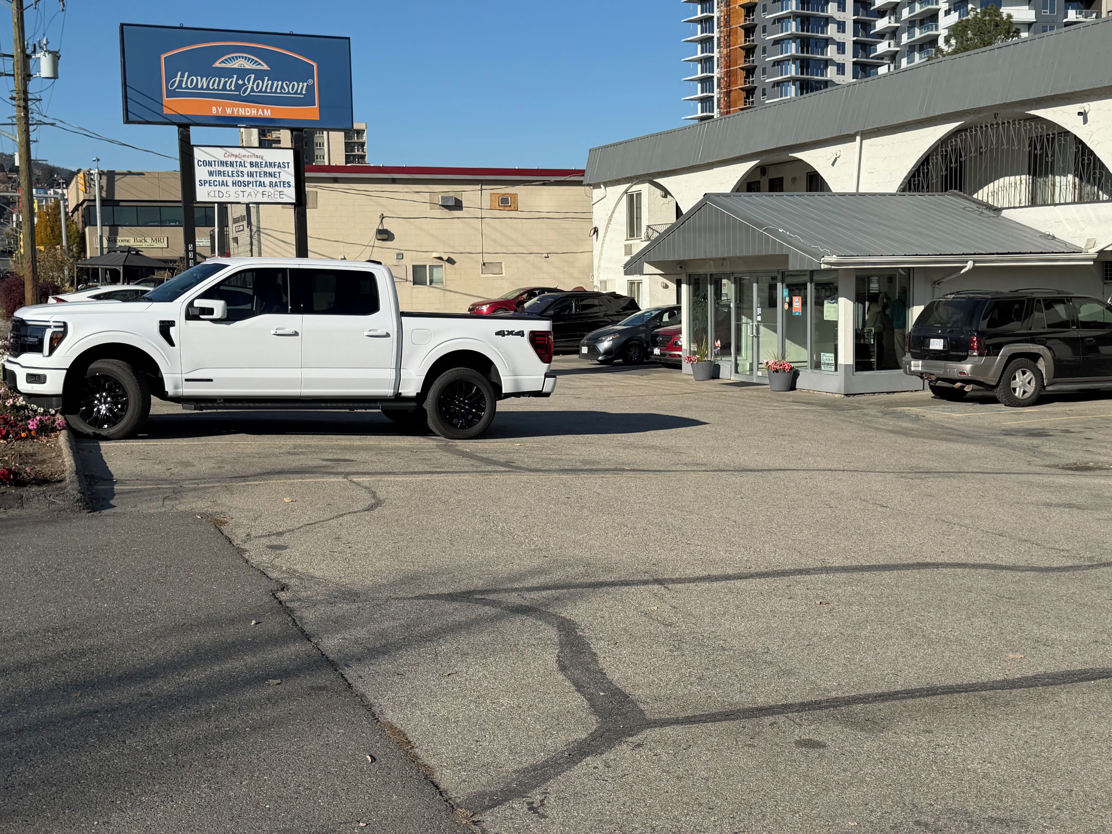 Un estacionamiento con una camioneta pickup blanca y una camioneta SUV negra. Hay un edificio con un letrero que dice 'Howard-Johnson By Wyndham'.