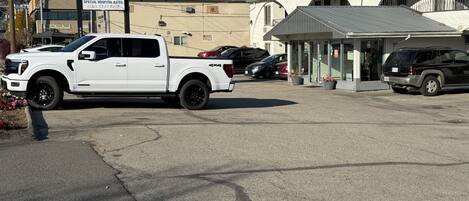 Un estacionamiento con una camioneta pickup blanca y una camioneta SUV negra. Hay un edificio con un letrero que dice 'Howard-Johnson By Wyndham'.
