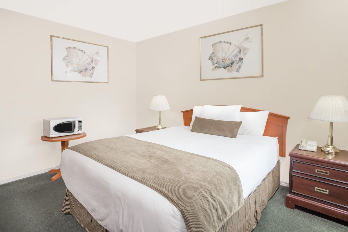 Een hotelkamer met een bed, nachtkastjes, een magnetron, lampen en kunstwerken aan de muren.