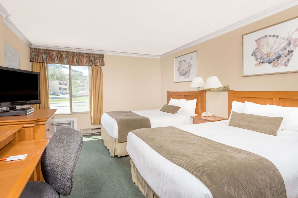 Een hotelkamer met twee bedden, een bureau met een televisie, een lamp en kunstwerken aan de muren.